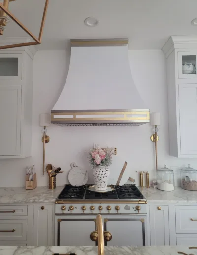 A kitchen with white cabinets and a gold hood.