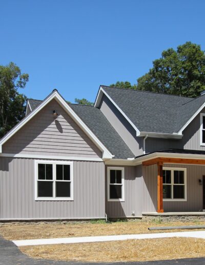 A modern, single-story house with a gabled roof and a detached garage, surrounded by trees under a clear blue sky.
