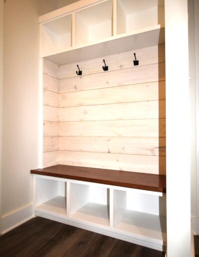 A mudroom with a wooden bench, three wall hooks, and open storage cubbies above and below.