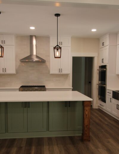Modern kitchen with a large island featuring green cabinets, pendant lights, stainless steel appliances, and white upper cabinets.