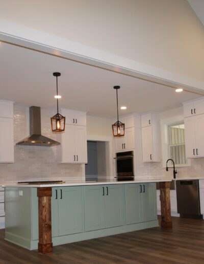 Modern kitchen with white cabinets, a large green island, stainless steel appliances, pendant lights, and wood flooring.